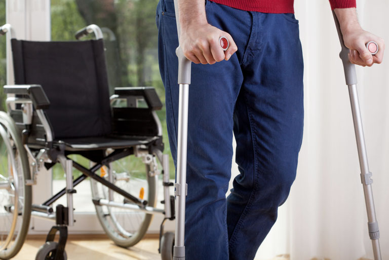 Mężczyzna o kulach na tle wózka inwalidzkiego